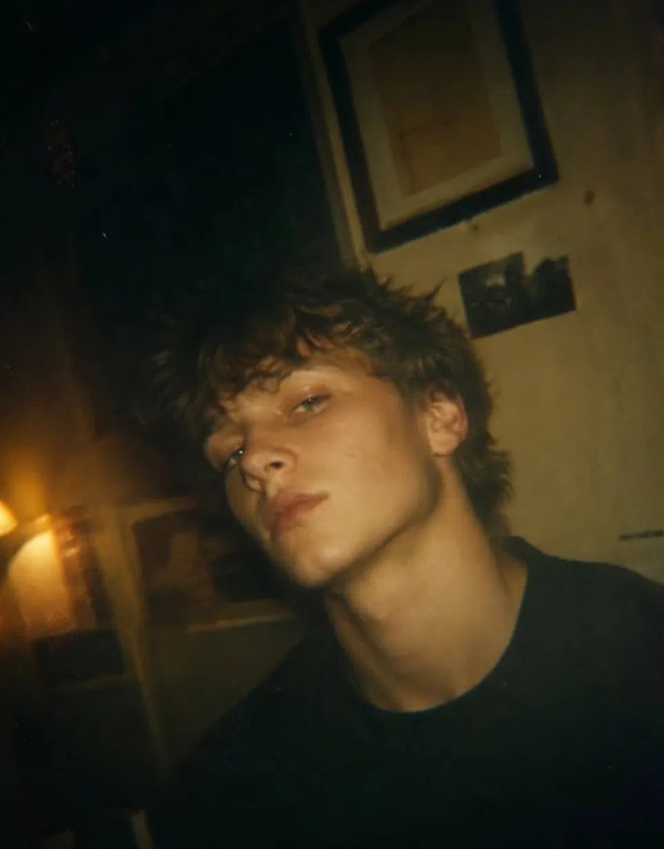 Moody cinematic portrait of a young man with dark curly hair in a dimly lit rustic room